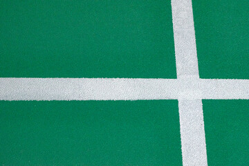 A minimalist, abstract shot capturing the bold white service lines intersecting on the bright green textured surface of a badminton court, representing structure, rules, and the field of play.