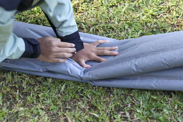 Diligent person deflating grey air mattress on grass. Focused individual preparing outdoor camping...