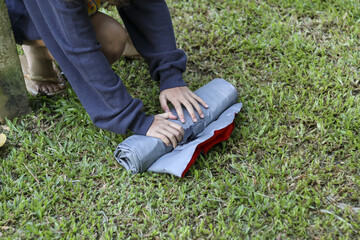 Focused person packing camping gear, carefully rolling grey sleeping pad or air mattress for tent....