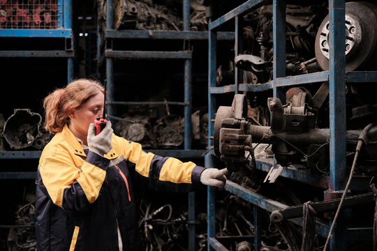 One Hispanic mature female inspector remotely works with walkie-talkie, checks auto spare parts stock in warehouse stack, operates jobs in manufacturing factory, and industrial worker occupation. - Powered by Adobe