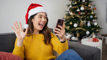 Happy young woman in a santa hat waving during a Christmas video call on her smartphone in a decorated home.
