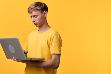 Young man in a yellow tee uses a laptop against a bright yellow backdrop, creating a modern tech...