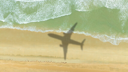 Aerial view of shadow passenger plane silhouette and sandy beach blue sea with waves at sea beach summer vacation sea travel concept	