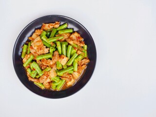 Stir-fried long bean curry with pork belly in a plate placed on a white blackground. Delicious Thai food.