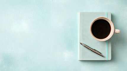 Overhead view of a pastel workspace featuring a closed blue notebook, pen, and black coffee cup.
