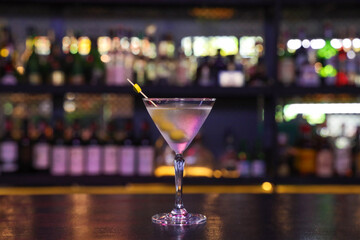 A vibrant martini cocktail with a lemon twist on a bar setting, surrounded by bottles. The classic drink is perfect for a night out. 