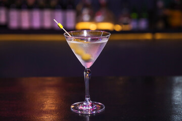A classic Martini cocktail, a symbol of sophistication. A clear Martini glass filled with the drink, garnished with olive. It's sitting on a table