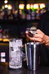 A bartender preparing a cocktail with a metal shaker and glass