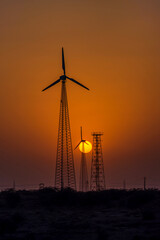 Obraz premium The setting sun with windmills silhouetted against an orange sky at Jaisalmer India.