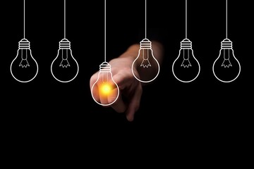 Creative ideas with light bulb concept on black background. Creative Innovation and business solutions. A hand touching yellow light bulb.