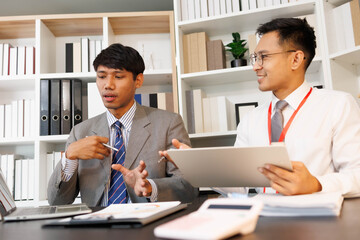 Two men are sitting at a desk, one of them is holding a piece of paper. They are having a conversation, and it seems like they are discussing something important. The atmosphere is tense
