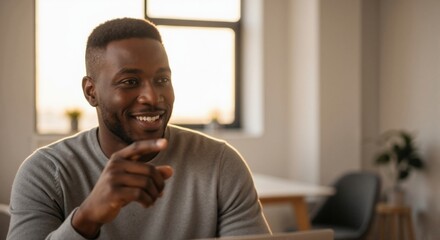 Happy young man in light sweater smiling and pointing with finger in modern bright office with blurred background, natural daylight, calm atmosphere