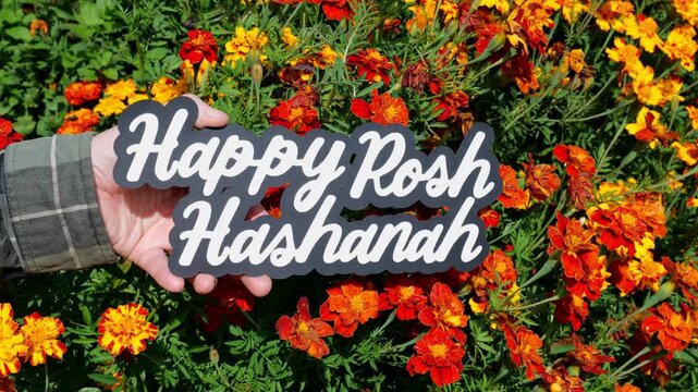 Person holds up the wording Happy Rosh Hashanah in front of Orange and Red Mums in the Garden in the Autumn Fall 4K Video Stock Footage