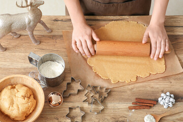 Woman rolling out gingerbread dough for Christmas cookies on table in kitchen, closeup