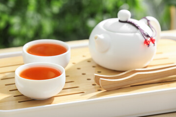 Tray with teapot and cups of tea on wooden table outdoors