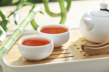 Tray with teapot, cups of tea and bamboo stems on wooden table outdoors