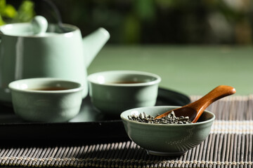 Tray with teapot, cups of tea and dry leaves on green table outdoors