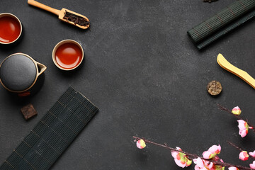 Teapot with cups of tea, dry pressed puer leaves, bamboo tongs and plum blossom branches on black...
