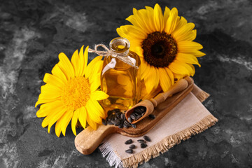 Wooden cutting board, bottle of sunflower oil and scoop of seeds on black grunge background, closeup