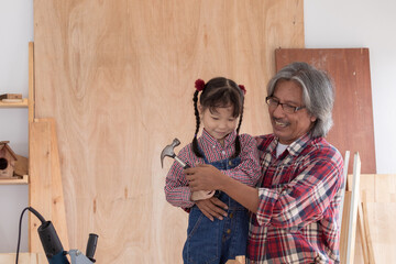 Asia retirement carpenter man spends time with cheerful granddaughter in carpentry studio, aged...