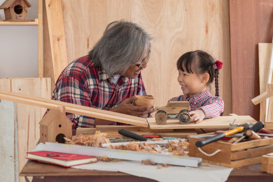 Carpenter family lifestyle activities concept, happy old age grandpa carpentry owner spends time with grandchild on holiday enjoy good relationship hobby and play together with adorable granddaughter - Powered by Adobe