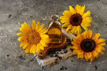 Wooden cutting board, bottle of sunflower oil and seeds on grey grunge background, closeup