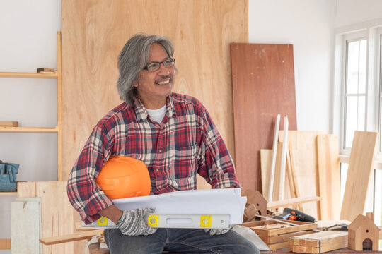  Elderly carpenter pointing at blueprint with confident look, expressing clarity, experience, and passion for creative construction during retirement life.Carpentry, man, blueprint, senior, focus.