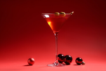 Glass of tasty red martini and Christmas balls on red background