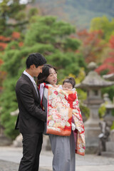 Fototapeta premium A man and woman are holding a baby in a red blanket. The baby is wrapped in a blanket and the couple is dressed in formal attire. The scene is likely a family portrait or a special occasion
