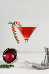 Glass of tasty red martini, Christmas ball and bartender tools on white background
