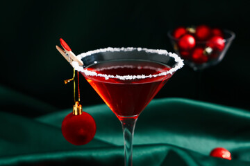 Glass of tasty red martini and Christmas ball on green fabric as background, closeup