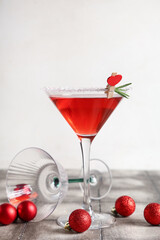 Glass of tasty red martini and Christmas balls on grey tile table near white wall
