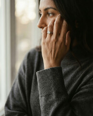 Pensive woman with diamond ring looking thoughtful by a window.