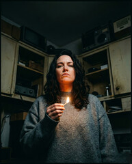 Woman's Face Lit by Match Flame in Dark Room