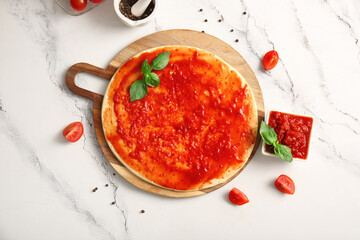 Board with raw dough for pizza and bowl of tasty tomato sauce on marble background