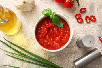 Bowl with tasty tomato sauce and ingredients on beige grunge background, closeup