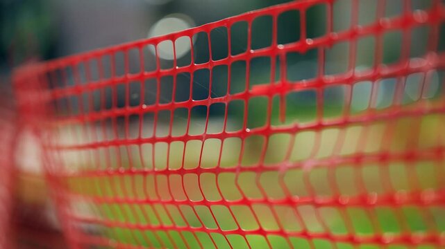 Close-up view of red plastic safety mesh fencing with shallow depth of field, perforated grid pattern and bokeh background, a temporary barrier for construction or crowd control