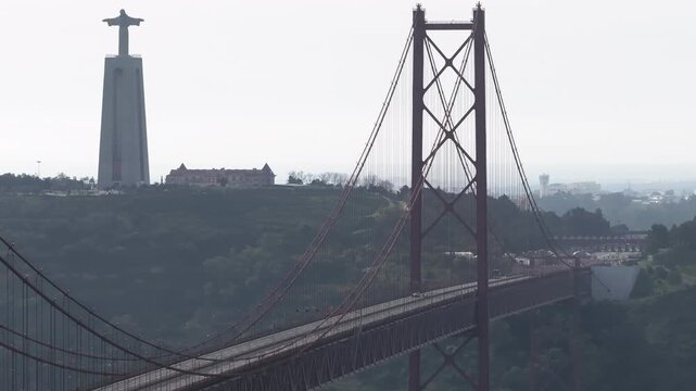 Aerial drone shot of lead cars guiding elite runners at the start of a major race on the red 25th April suspension bridge in Lisboa, Portugal, with Cristo Rei in the background
