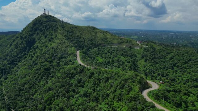 An aerial push of People's Park in the Sky showing forested hills, winding road, and mountaintop towers in Tagaytay, Cavite, Philippines