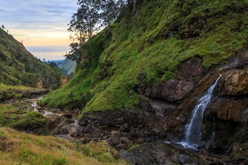 Waterfall and Stream Flowing Through a Steep, Lush Green Valley