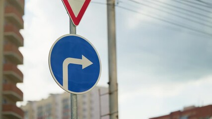 Urban intersection with a blue circular mandatory right turn traffic sign and arrow, overhead wires, and nearby buildings, emphasizing road regulations and directional guidance.