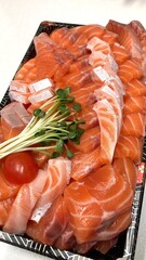 Fresh salmon sashimi arranged neatly on a plate with vibrant orange slices and delicate marbling, accompanied by garnish such as shredded radish and green leaves, creating a visually appealing