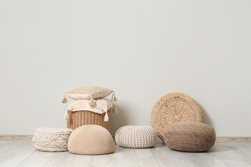 Different stylish poufs and wicker table with soft pillows near grey wall in room