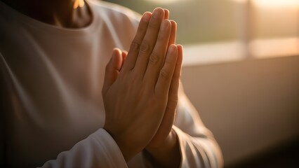 Close-up of hands clasped together in prayer, illuminated by warm sunlight.