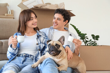 Young couple with cups of coffee and French bulldog sitting in rented apartment on moving day