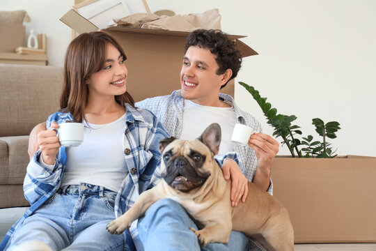Young couple with cups of coffee and French bulldog sitting in rented apartment on moving day - Powered by Adobe