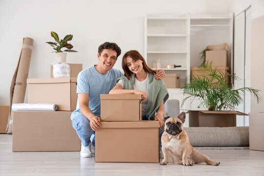 Happy young couple with dog and cardboard boxes in rented apartment on moving day