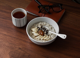 Delicious breakfast - oatmeal porridge with banana, caramel, chocolate and a glass of coffee on a wooden table