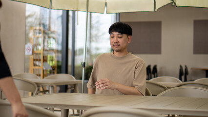 Man sitting alone at an outdoor cafe table, waiting calmly in a relaxed dining environment.