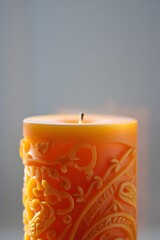 Ornate orange candle with burning wick in soft light studio photography setting
